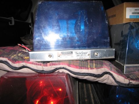 1991 Ford LTD Crown Victoria - Federal Twin Sonic blue emergency beacon rests on a plaid blanket with red and blue beacon lights visible below it.