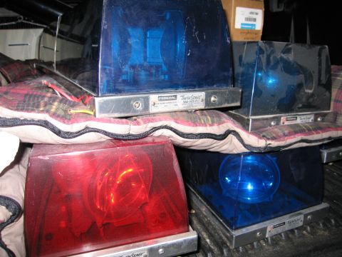 1991 Ford LTD Crown Victoria - Four red and blue Federal Twin Sonic emergency beacon lights stacked on plaid blankets, with a cardboard box behind them.