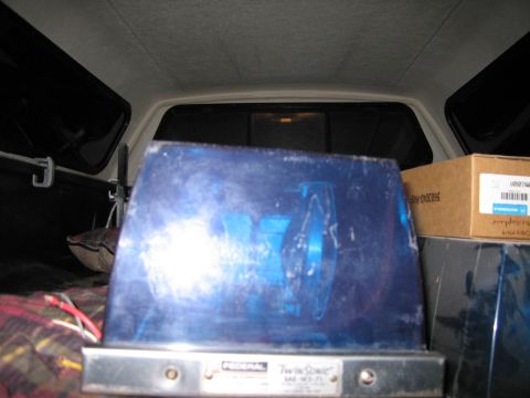 1991 Ford LTD Crown Victoria - Federal Twin Sonic blue emergency beacon stands upright in a pickup bed beside a cardboard box, with the cab interior behind.