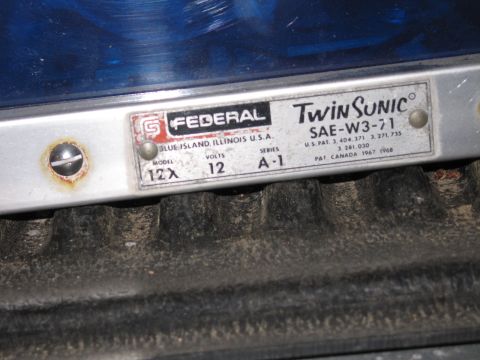1991 Ford LTD Crown Victoria - Close-up of a Federal Twin Sonic model 12X, 12 volt, SAE-W3-71 nameplate on a blue emergency beacon in a truck bed.