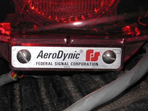 1991 Ford LTD Crown Victoria - Federal Signal Corporation AeroDynic nameplate mounted below a glowing red emergency beacon light in a truck bed.