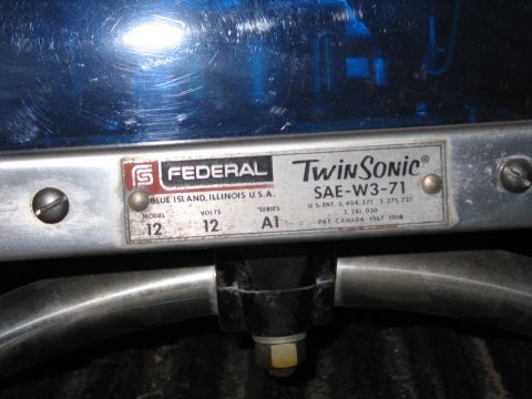 1991 Ford LTD Crown Victoria - Close-up of a Federal Twin Sonic model 12, 12 volt, SAE-W3-71 nameplate on the chrome base of a blue emergency beacon.
