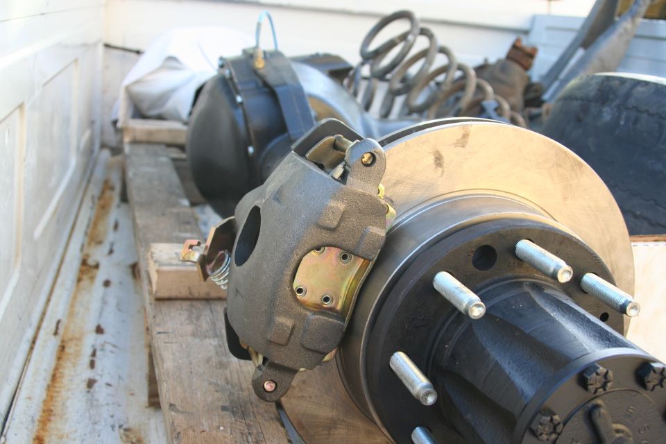 Rear axle assembly with disc brake caliper and rotor, sitting on wooden planks in a truck bed