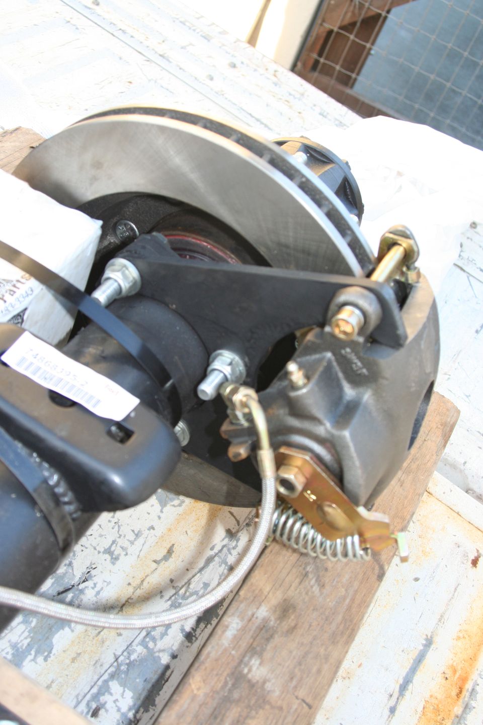 Rear disc brake assembly with caliper, rotor, and mounting bracket on wooden planks