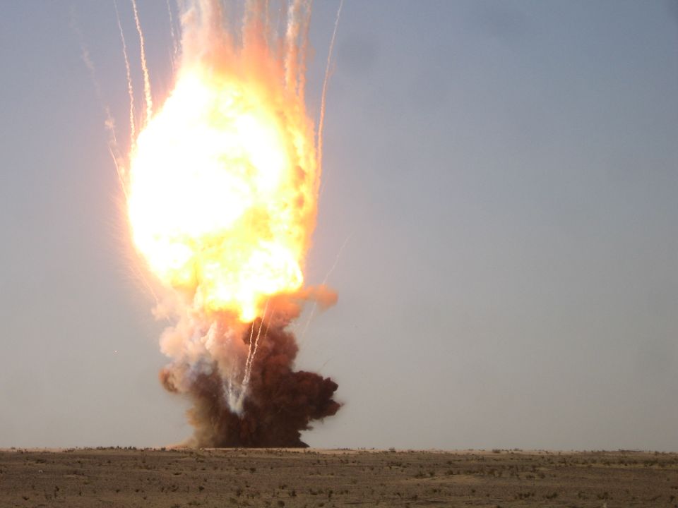 Explosion with debris and smoke against a clear sky over a desert landscape