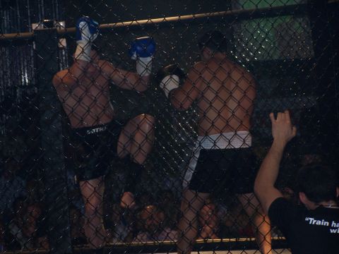 1979 Ford F-150 - Two fighters engage in a bout within a cage, observed through a wire mesh barrier.