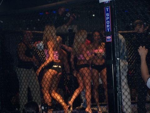 1979 Ford F-150 - Ring girls stand in a cage during a fight event, with a sign reading 'TSPORT' visible.