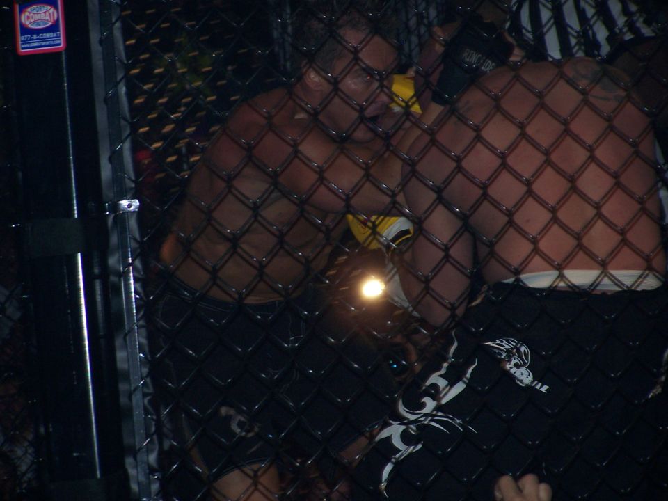 Dim photo of MMA fighters clinched against a cage fence