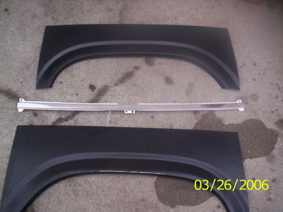 Two black truck fender panels and a chrome trim strip laid out on a driveway