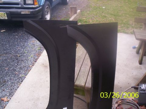 1988 Ford Bronco - Two black fender patch panels sit on concrete next to a blue truck.