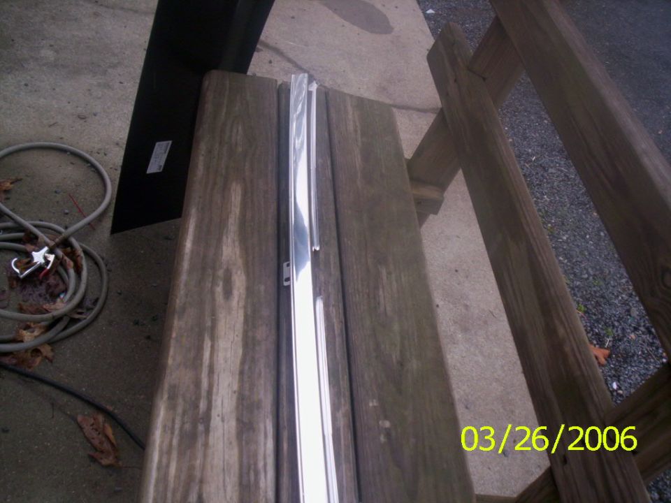 Chrome trim piece on wooden surface with coiled hose and date stamp