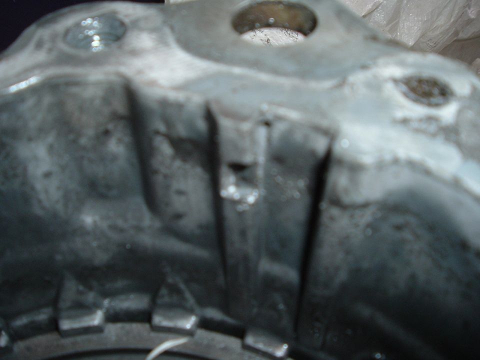 Close-up of a cast metal housing with bolt holes and an apparent crack in the ribbed casting