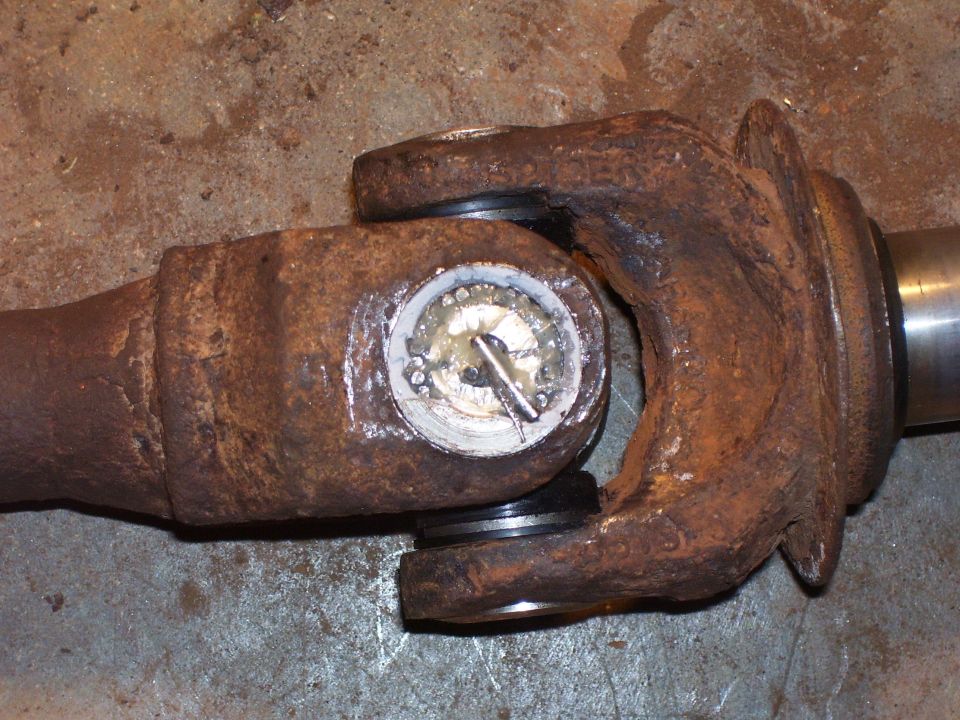 Rusty driveshaft yoke with U-joint bearing cap removed showing greased needle bearings