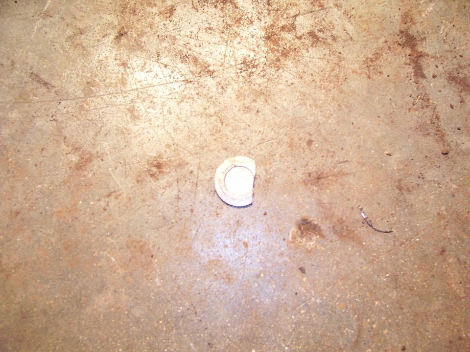 Small white round plastic cap or bushing on a stained concrete garage floor