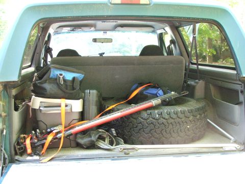 1996 Ford Bronco - The rear storage area of a vehicle is filled with various items, including a spare tire and a long pole.