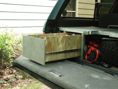 1996 Ford Bronco - Custom wooden drawer installed in the rear storage area of an SUV, next to a spare tire.