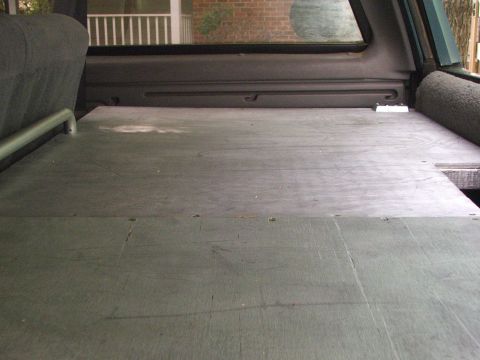1996 Ford Bronco - The rear storage area of a 1996 Ford Bronco features a custom wooden floor panel and a metal grab handle.