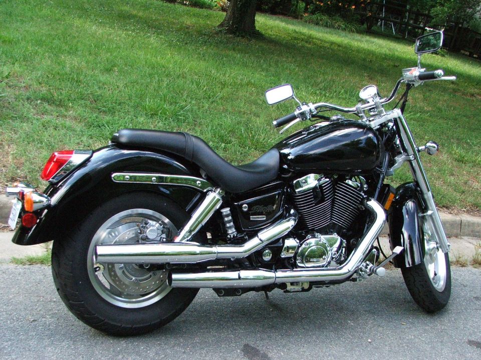 Black Honda Shadow cruiser motorcycle, right side view with chrome exhaust, parked by grass