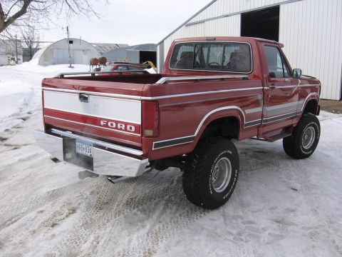 1984 Ford F-150 - This red Ford pickup truck is seen from the rear in a snowy outdoor setting with buildings in the background.