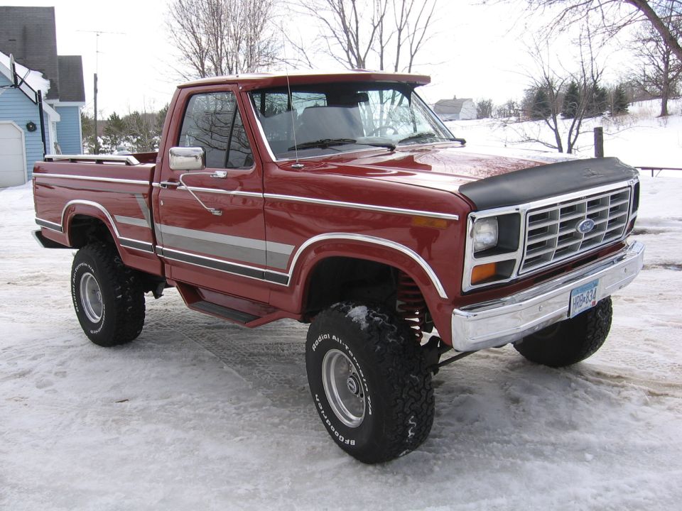 Red Ford pickup truck with silver side stripes, lifted suspension, and aftermarket wheels parked in snow