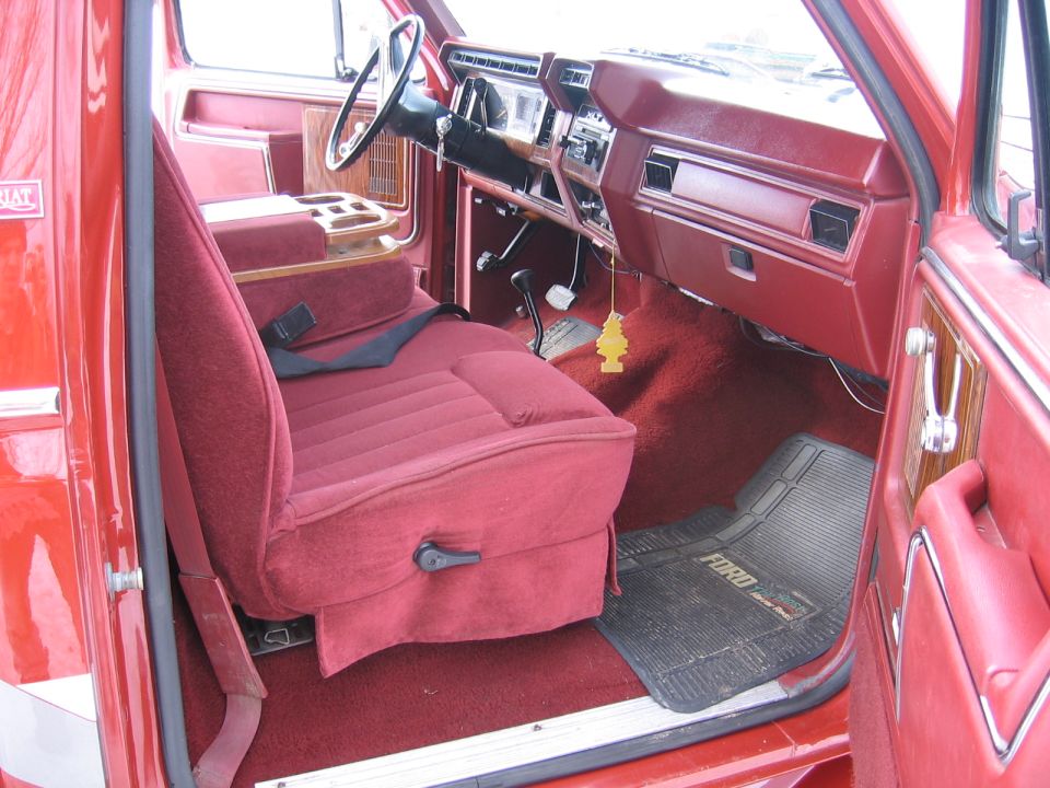 Interior of a red Ford truck showing the driver's seat, dashboard, and floor mat with 'FORD' text