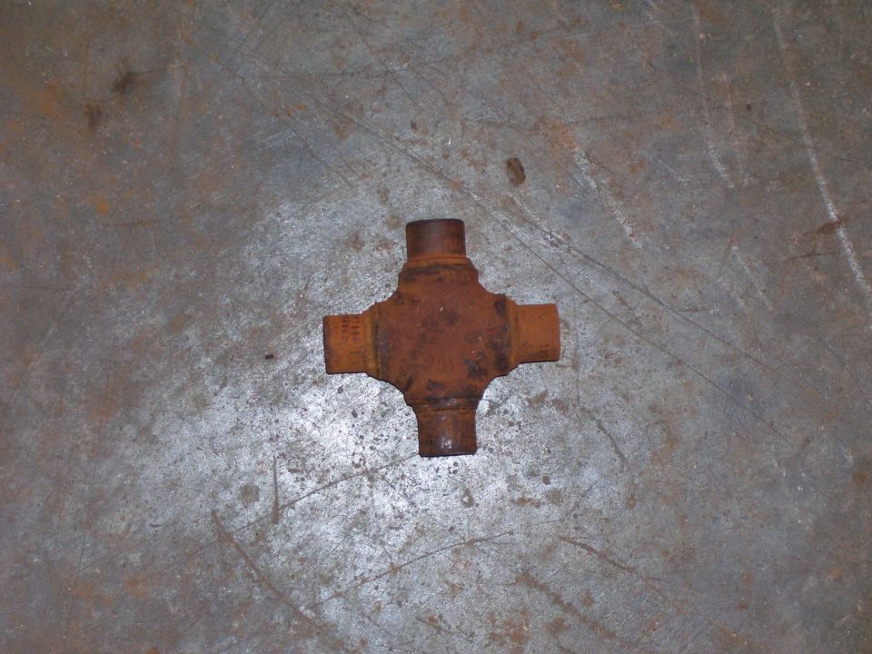 Rusty universal joint cross with four bare trunnions lying on a concrete floor