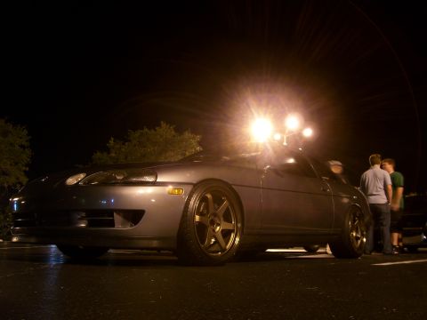 1994 Ford Probe - A gray coupe with aftermarket bronze wheels is parked at night under bright lights.