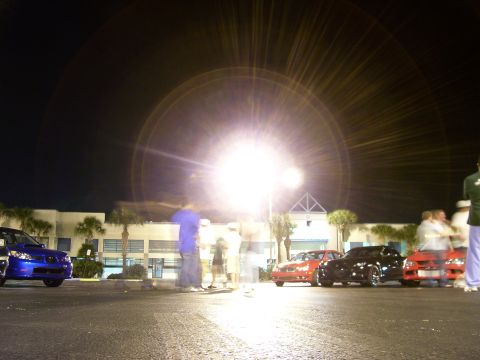 1994 Ford Probe - Several cars and people are visible in a parking lot at night, illuminated by a bright light.