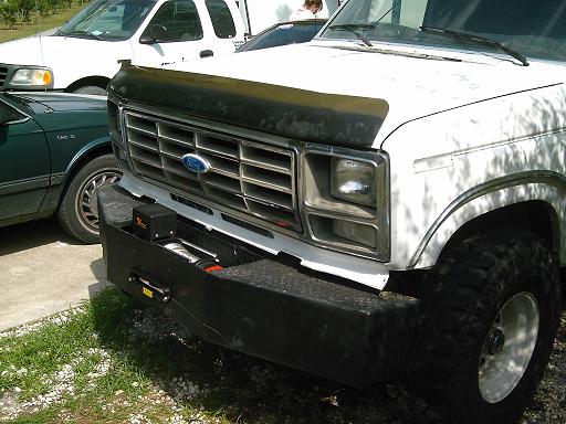 1986 Ford Bronco front end with winch plate bumper. Green car and white truck visible