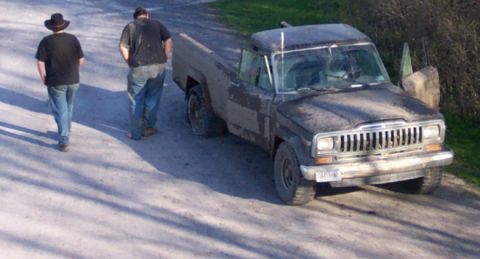 1979 Ford F-150 - A muddy Jeep Comanche pickup truck is parked on a dirt road with two people walking away from it.