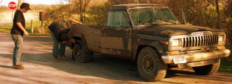 1979 Ford F-150 - Two people attend to a flat tire on a muddy 1979 Jeep J-10 pickup truck.