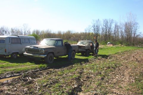 1979 Ford F-150 - Several muddy vehicles are parked in a grassy field with trees in the background.