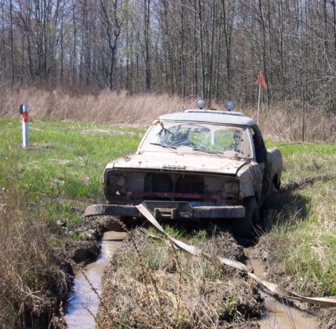 1979 Ford F-150 - A mud-caked Dodge pickup truck is stuck in a muddy rut, with a tow strap attached to its front bumper.