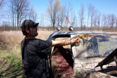 1979 Ford F-150 - Man interacts with a muddy truck in a field, holding a corn cob.