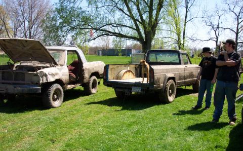1979 Ford F-150 - Two pickup trucks, covered in mud, are parked on a grassy field with people standing nearby and a dog in the bed of one truck.