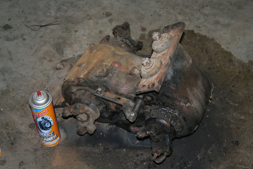 Removed rusty transfer case or differential on garage floor beside brake cleaner