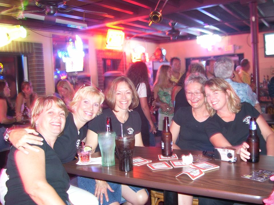 Four women smiling and sitting at a bar with drinks and beer bottles on the table