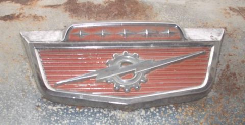 1965 Ford F-100 - This emblem features a stylized lightning bolt crossed with a gear-like shape on a red, ribbed background.