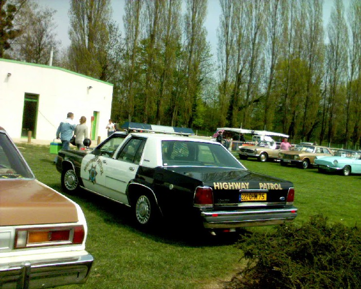 Black and white Highway Patrol Crown Victoria parked on grass at a car meet, rear three-quarter