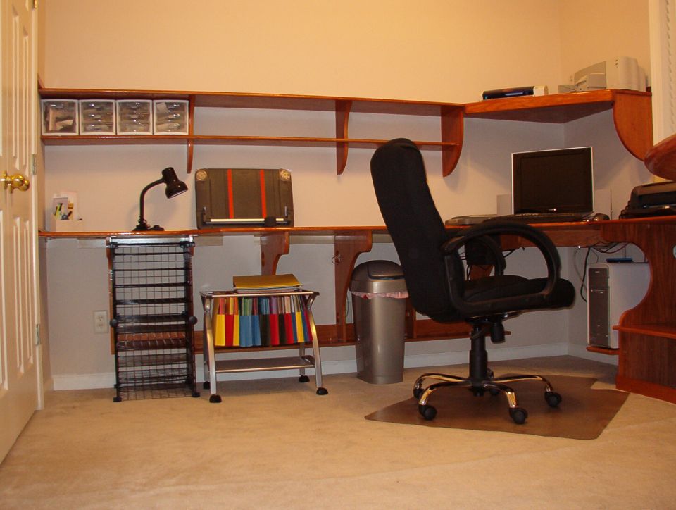 Home office corner with wood floating shelves, black desk chair, laptop and file cart
