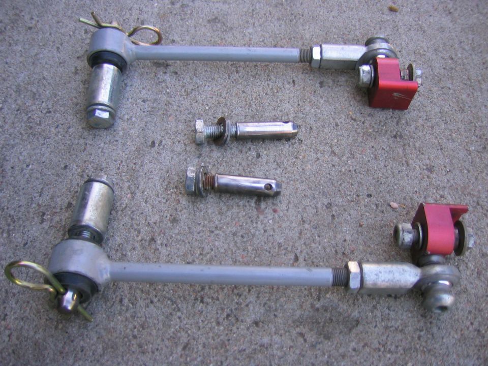 Pair of adjustable quick-disconnect sway bar links with red brackets and pins on concrete