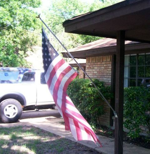 1993 Ford Bronco - A U.S. flag hangs from an angled pole on the porch post of a brick house, with a white pickup truck wearing a matching white camper shell p…
