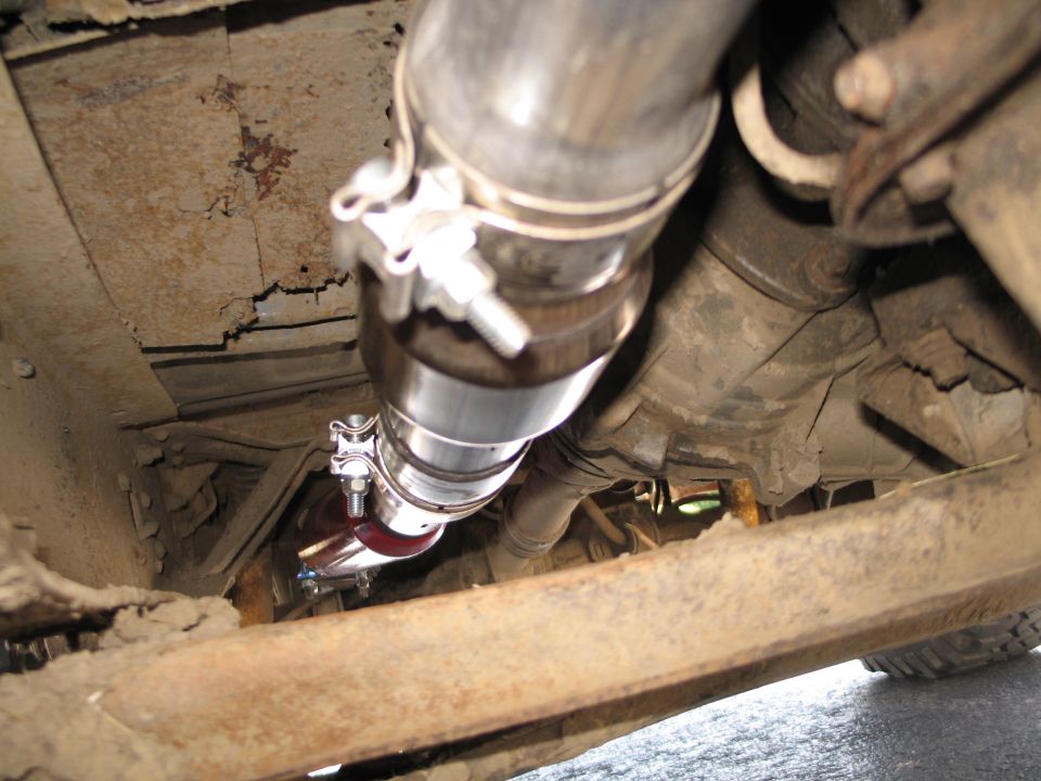 New stainless exhaust pipe and red poly hanger bushing under a rusty truck frame