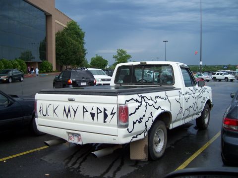 1983 Ford Bronco - A white pickup truck is parked in a lot, custom lightning bolt graphics and text on its tailgate.