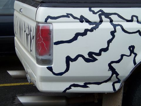 1983 Ford Bronco - Pickup truck tailgate with custom lightning graphics and visible text. Exhaust pipes are prominent.