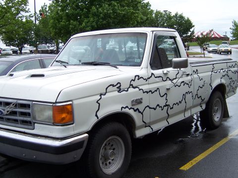 1983 Ford Bronco - A white Ford F-150 pickup truck is parked in a lot, unique black line art graphics along its body.