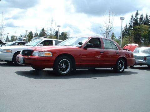 1999 Ford Crown Victoria - Three sedans are parked in a lot under a cloudy sky. One is red, one is white, and one is light blue.