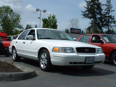 1999 Ford Crown Victoria - A white Ford Crown Victoria is parked in a lot, with a red car visible to its right.