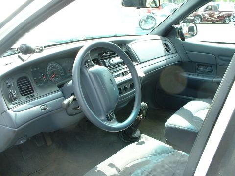 1999 Ford Crown Victoria - The interior of a police car is shown, with a visible dashboard, steering wheel, and seats. A police light is mounted on the dash.
