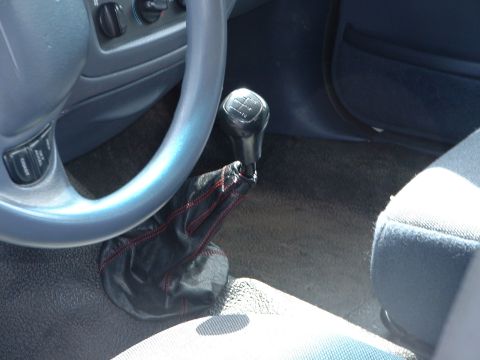 1999 Ford Crown Victoria - Interior view of a car's manual transmission shifter and steering wheel, with a black leather boot and red stitching.
